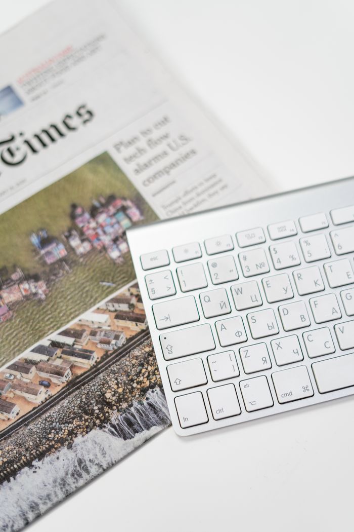 gallery-1 A white keyboard and newspaper on a desk, ideal for home office or freelance work environments.
